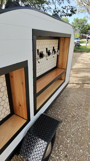 Mobile bar trailer with four beer taps, honeycomb tile backsplash and wooden shelves, parked on a gravel driveway under trees
