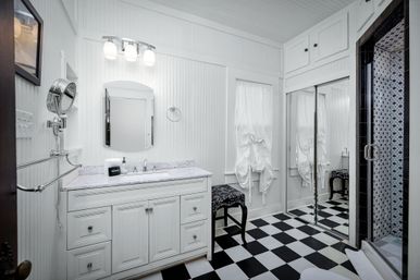 Bright white bathroom interior with marble-top vanity, arched mirror, retro black-and-white checkered floor and glass shower with hexagon mosaic tile