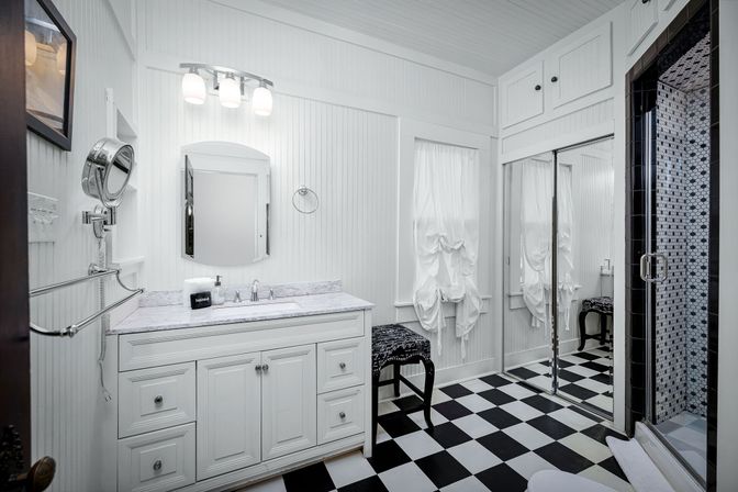 Bright white bathroom interior with marble-top vanity, arched mirror, retro black-and-white checkered floor and glass shower with hexagon mosaic tile