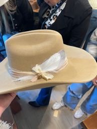 Tan wide-brim felt hat with pale ribbon and white feather accent, boho-western style displayed in a boutique setting