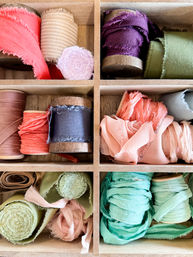 Neat wooden cubby filled with colorful frayed silk and cotton ribbons on spools — coral, peach, mint, olive, navy and purple craft ribbons for sewing, wrapping and DIY projects.