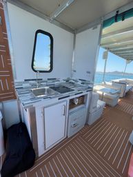 Pontoon boat galley with stainless sink, cooktop, mini fridge, cushioned seating and sunny water view.