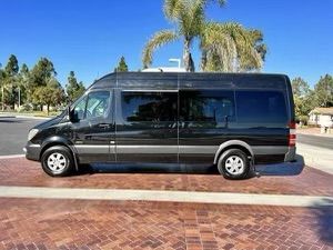 Black passenger van parked on red brick plaza under palm trees on a sunny suburban street