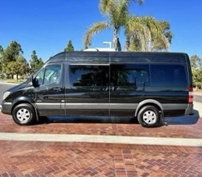 Black passenger van parked on red brick plaza under palm trees on a sunny suburban street
