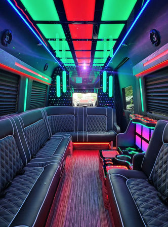 Club-style party bus interior with quilted black leather lounge seating, multicolor LED ceiling panels and neon accent lighting for nightlife events