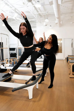 Instructor adjusting a woman on a Pilates reformer during a small group reformer class in a bright modern fitness studio