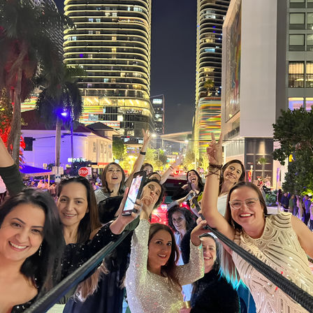 Group of smiling women celebrating and taking a selfie on a lively downtown street at night with palm trees and illuminated modern high-rise buildings — urban nightlife scene