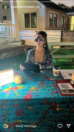 Evening patio scene: a glittery-clad reader wearing stacked sunglasses sits behind a bright floral tablecloth, holding a tablet with a lightbox reading sign, takeaway coffee cup and QR code on the table.
