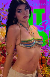 Close-up of a dark-haired model with glitter makeup wearing a rainbow beaded bikini top, layered necklaces and gold body chains against a neon tropical floral backdrop with oranges — festival fashion vibe.