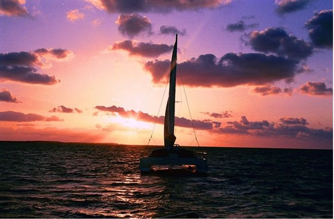 Silhouette of a sailboat on the open ocean at a vivid purple-orange sunset with glowing clouds