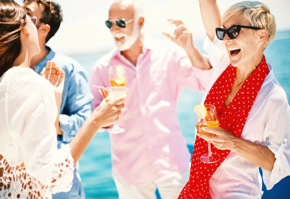 Sunny summer boat party on blue ocean — friends laughing and toasting cocktails; woman in red polka-dot scarf and sunglasses raises a drink.