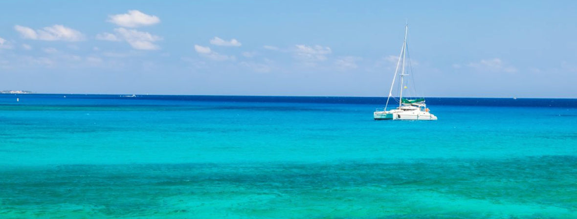 White catamaran drifting on vibrant turquoise tropical sea under a clear blue sky, perfect island-sailing and beach vacation scene.