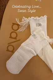 White lace-trimmed bridal ankle socks with ruffled cuffs and silver "I DO" embroidery, textured non-slip honeycomb soles, staged on a tan background with "Celebrating Love Swan Style" text.