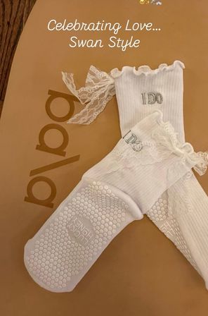White lace-trimmed bridal ankle socks with ruffled cuffs and silver "I DO" embroidery, textured non-slip honeycomb soles, staged on a tan background with "Celebrating Love Swan Style" text.