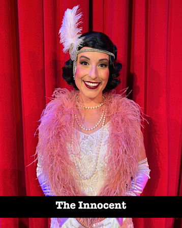 Smiling stage performer in a 1920s flapper costume—black bob wig, rhinestone headband with white feather, pink feather boa, pearl necklaces—posing in front of a red theater curtain with the caption “The Innocent”.