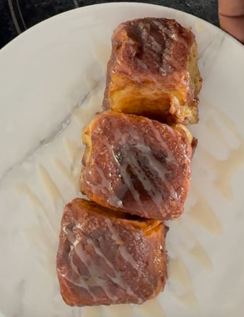 Three square cinnamon-sugar glazed pull-apart pastries drizzled with icing on a white marble plate — close-up breakfast pastry