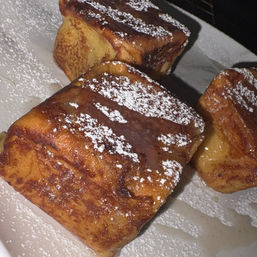 Close-up of golden French toast cubes dusted with powdered sugar and drizzled with maple syrup on a white plate — indulgent breakfast or brunch