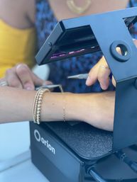 Close-up of a wrist with layered gold bracelets and a delicate chain being worked on under a jeweler's lamp, artisan using pliers at a jewelry workbench.