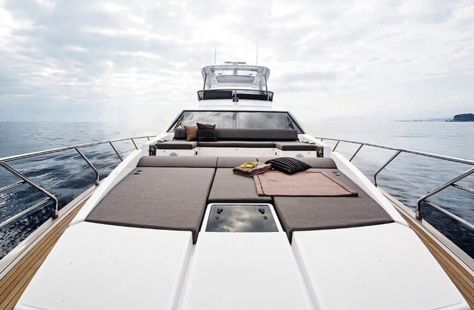 Luxury yacht sun deck with cushioned loungers, pillows and a blanket overlooking calm open sea under an overcast sky