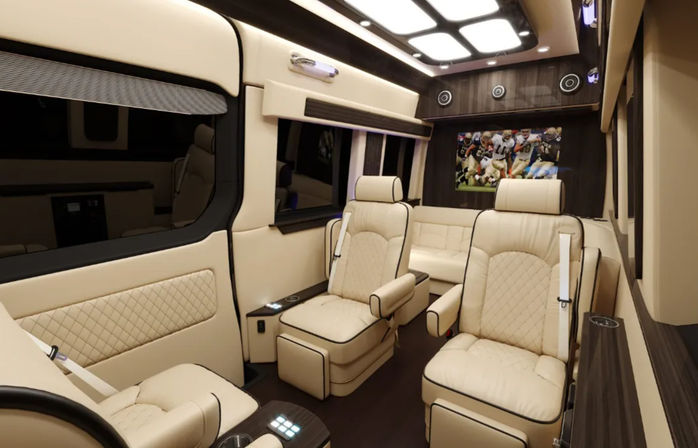 Luxury conversion van interior with cream leather reclining captain seats, wood veneer trim, ambient LED ceiling lights and a wall-mounted TV showing a football game.