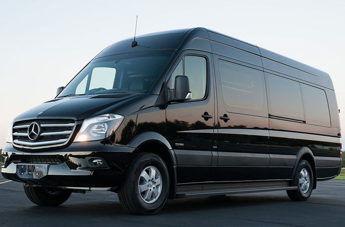 Glossy black Mercedes-Benz Sprinter passenger van parked on asphalt at dusk, showing front grille, alloy wheels and tinted side windows