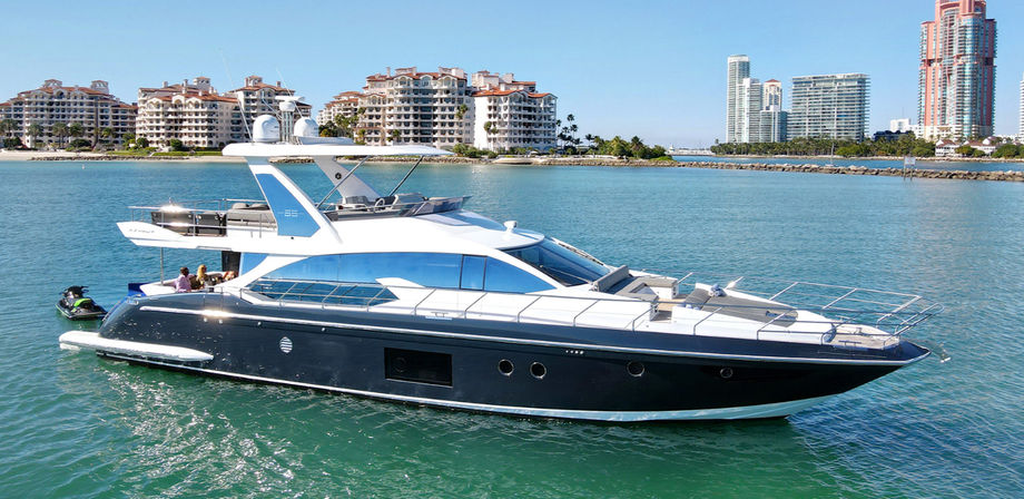 Sleek black-and-white luxury motor yacht on turquoise water near a shoreline with beachfront condos and high-rise buildings under a clear blue sky