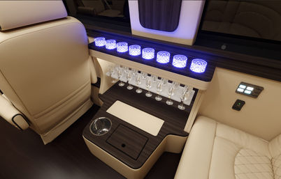 Luxury vehicle interior with cream leather seats, dark wood minibar console, row of blue LED‑lit glasses and hanging wine goblets—stylish bar-ready VIP travel cabin.