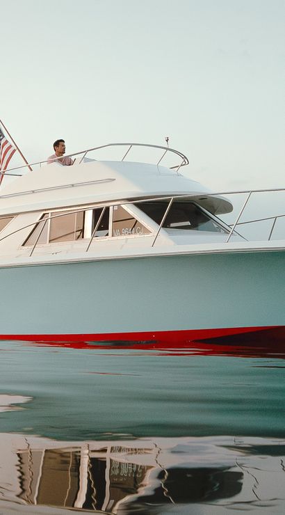 Light-blue motor yacht with a red waterline and American flags on bow and stern floating in a calm coastal harbor at dusk, crisp water reflection