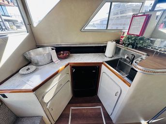 Cozy yacht galley with marble countertop, stainless sink, mini fridge, ice bucket and fruit bowl under porthole windows with marina view