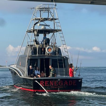 Rear view of a sportfishing boat with a tall observation tower, anglers and passengers on the stern holding multiple fishing rods, cruising in calm coastal waters under a clear blue sky.
