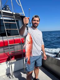 Proud angler on a fishing boat holding a freshly caught red snapper against a clear blue sky and open ocean