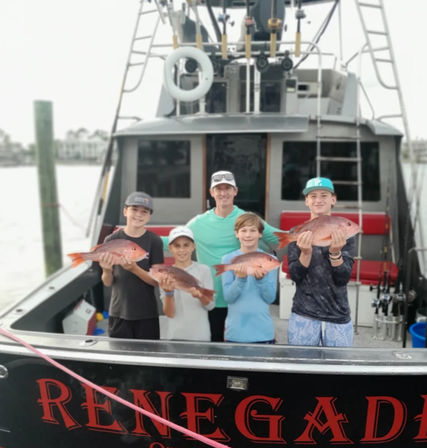 Five anglers smiling on a docked fishing boat at a marina, each holding a red snapper they caught on a coastal fishing trip.