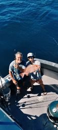 Two anglers on a boat deck proudly holding a freshly caught red snapper over deep blue offshore ocean water