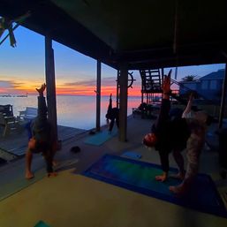 Sunset yoga on a covered waterfront dock, silhouettes stretching on mats with a vibrant pink-orange sky reflecting on calm bay waters
