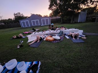 Backyard at sunset with a small group reclining on mats and cushions around a low table with candles, bowls and blankets for an outdoor relaxation session