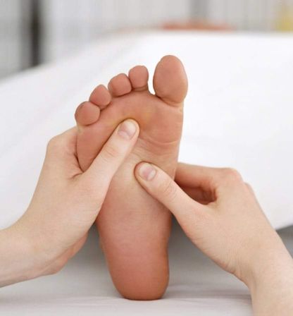 Close-up of hands giving a soothing foot massage, thumbs applying reflexology pressure to the bare sole on a white sheet — spa-style foot therapy for relaxation and pain relief.