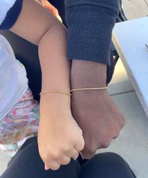 Close-up of two wrists side by side wearing matching delicate gold chain bracelets, fists touching — a simple, stylish symbol of connection.