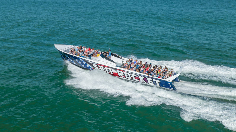 High-speed boat tour with a star-spangled hull carrying passengers across blue ocean, kicking up a foamy white wake