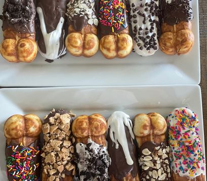 Close-up of two white plates with a colorful assortment of dipped bubble‑waffle sticks — chocolate and vanilla glazes topped with rainbow sprinkles, chopped nuts, crushed cookies and candies, gourmet dessert