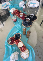 Vibrant outdoor patio brunch spread with a turquoise runner and fruit charcuterie boards of strawberries, raspberries, blueberries, blackberries, mini marshmallows, chocolate dip and sprinkles.