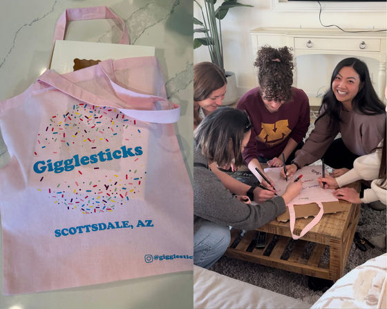 Pink canvas tote with colorful sprinkle donut graphic on a countertop, and a group of friends gathered around a living-room coffee table happily signing and decorating the tote