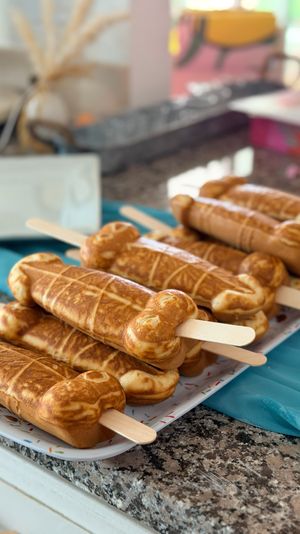 Golden-brown waffle pops on wooden sticks stacked on a tray over a granite kitchen counter – playful party dessert display