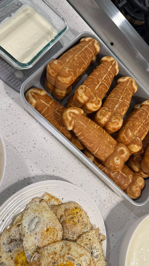 Home kitchen breakfast on a white quartz countertop: tray of golden tubular waffle sticks, plate of peppered fried eggs, bowl of scrambled eggs and bowls of yogurt or cream by the stove.