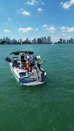 Friends on a wakeboarding boat in turquoise water with the Miami skyline and sunny blue sky