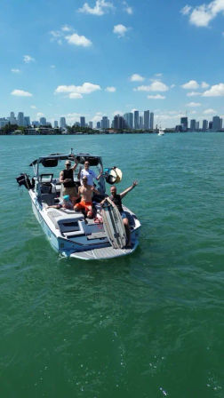 Friends on a wakeboarding boat in turquoise water with the Miami skyline and sunny blue sky