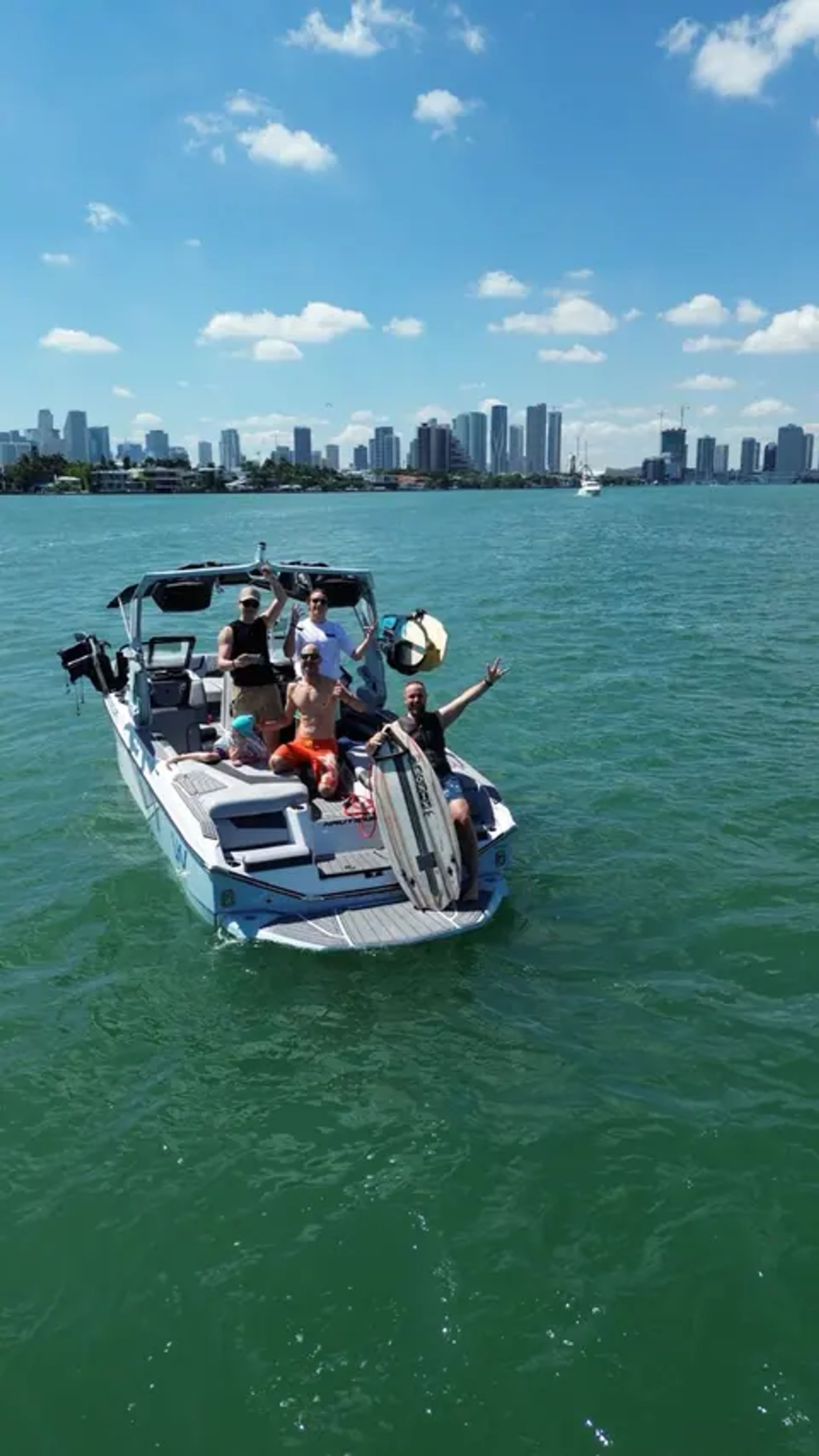 Friends on a wakeboarding boat in turquoise water with the Miami skyline and sunny blue sky