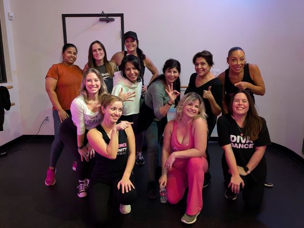 Happy post-dance class group of women posing and smiling in an indoor dance fitness studio, wearing athletic outfits and sneakers.