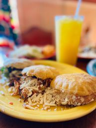 Savory Latin American corn cakes (arepas) filled with shredded chicken and crumbled white cheese on a bright yellow plate, with a blurred tall glass of orange juice in the background.