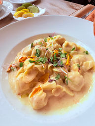 Creamy cheese tortellini in a silky sauce topped with microgreens and edible flower petals on a white plate, with lemon and lime wedges on the side — elegant Italian restaurant pasta.