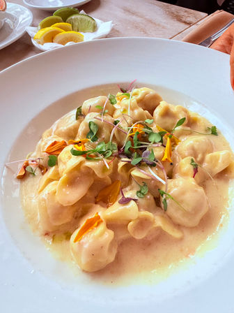Creamy cheese tortellini in a silky sauce topped with microgreens and edible flower petals on a white plate, with lemon and lime wedges on the side — elegant Italian restaurant pasta.